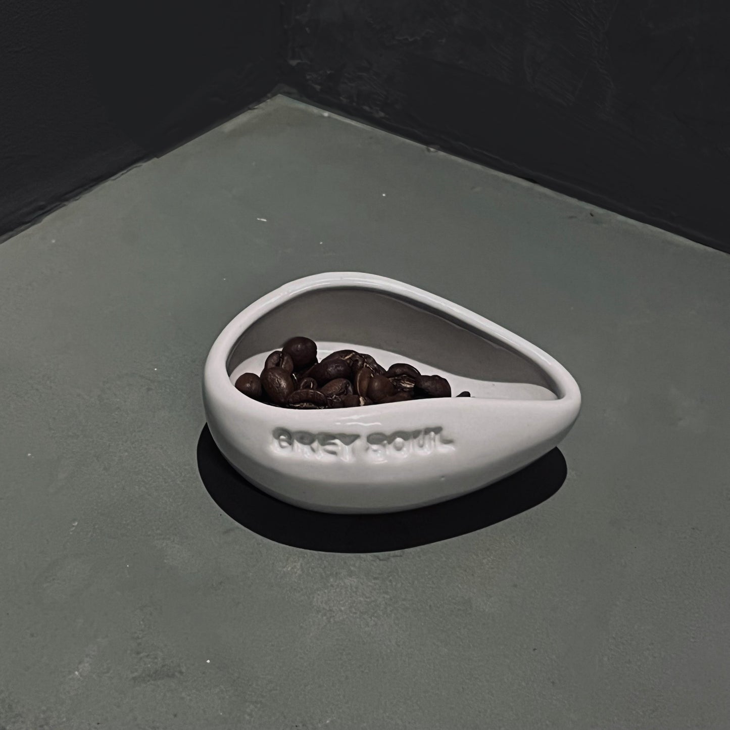 A white stoneware matte coffee bean doser with the brand 'GREY SOUL' embossed on the side, filled with coffee beans.