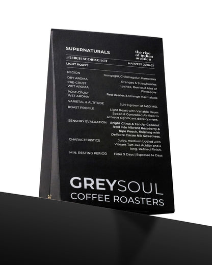 A black coffee roaster information card or label for Greysoul Coffee Roasters, featuring white text detailing the Supernaturals blend, roast details, and sensory evaluation, shown standing on a black surface against a white background.