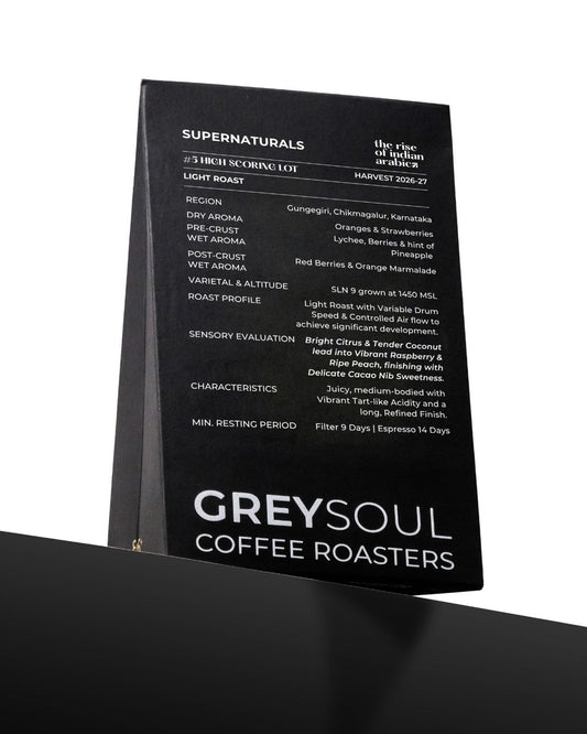 A black coffee roaster information card or label for Greysoul Coffee Roasters, featuring white text detailing the Supernaturals blend, roast details, and sensory evaluation, shown standing on a black surface against a white background.